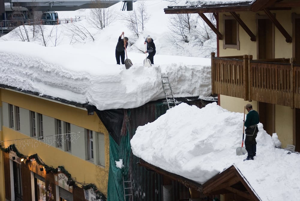 Two men shoveling snow off a roof