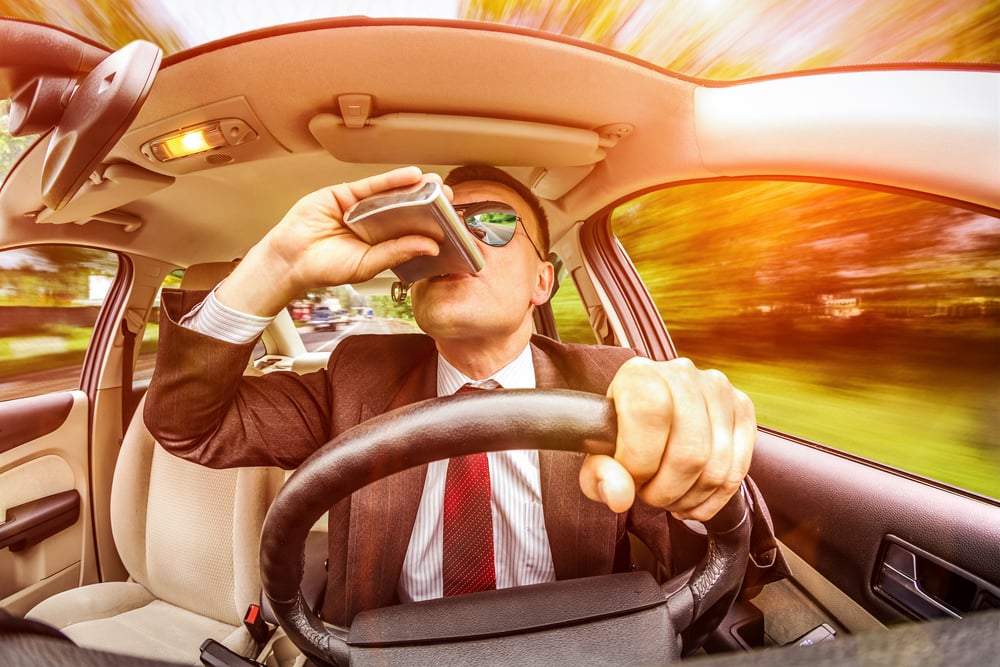 Man drinking from flask behind wheel of car