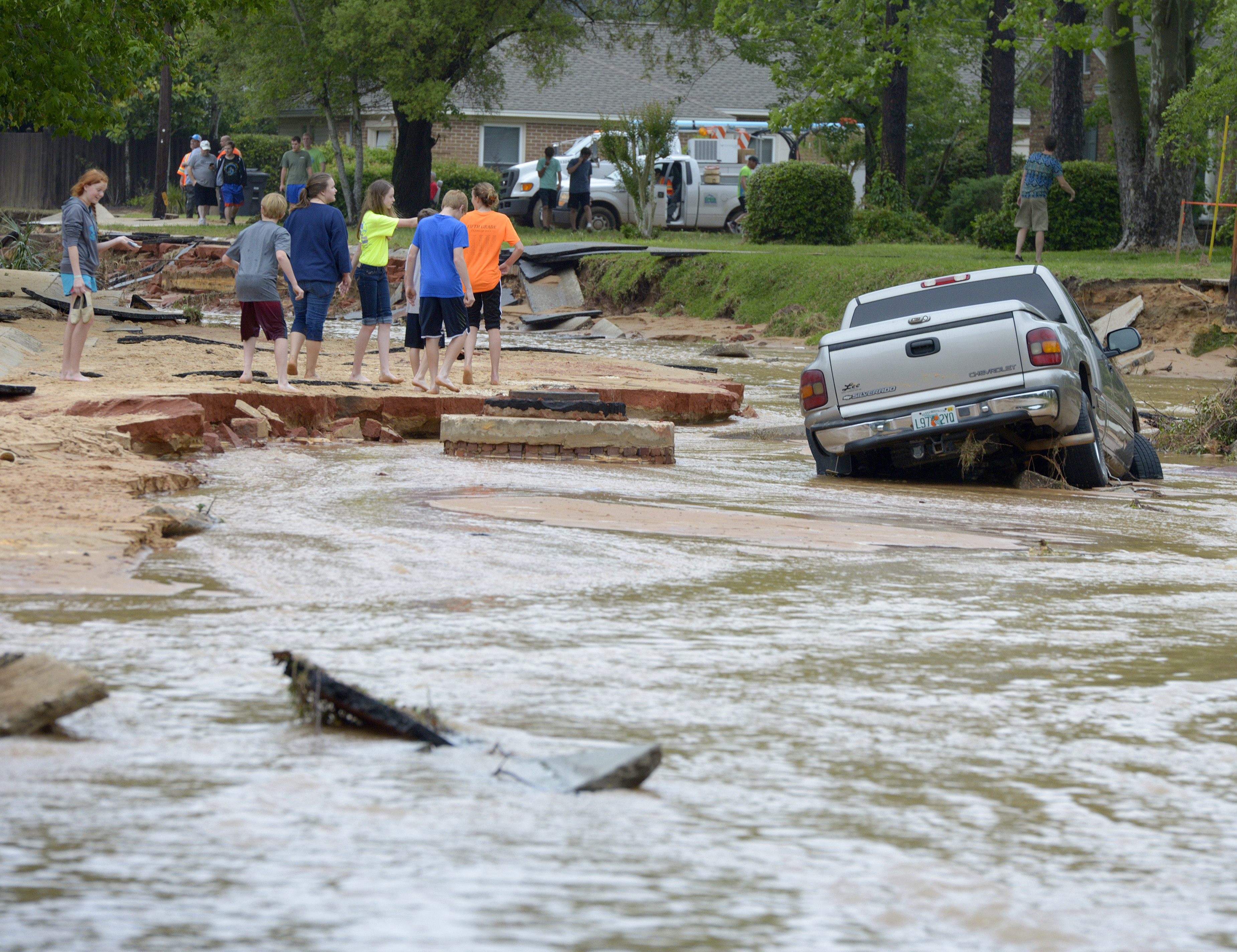 Residents walk near a truck stuck in deep water and mud on Piedmont Street after flood-water damage caused by torrential rains in Pensacola, Fla., Wednesday, April 30, 2014. 