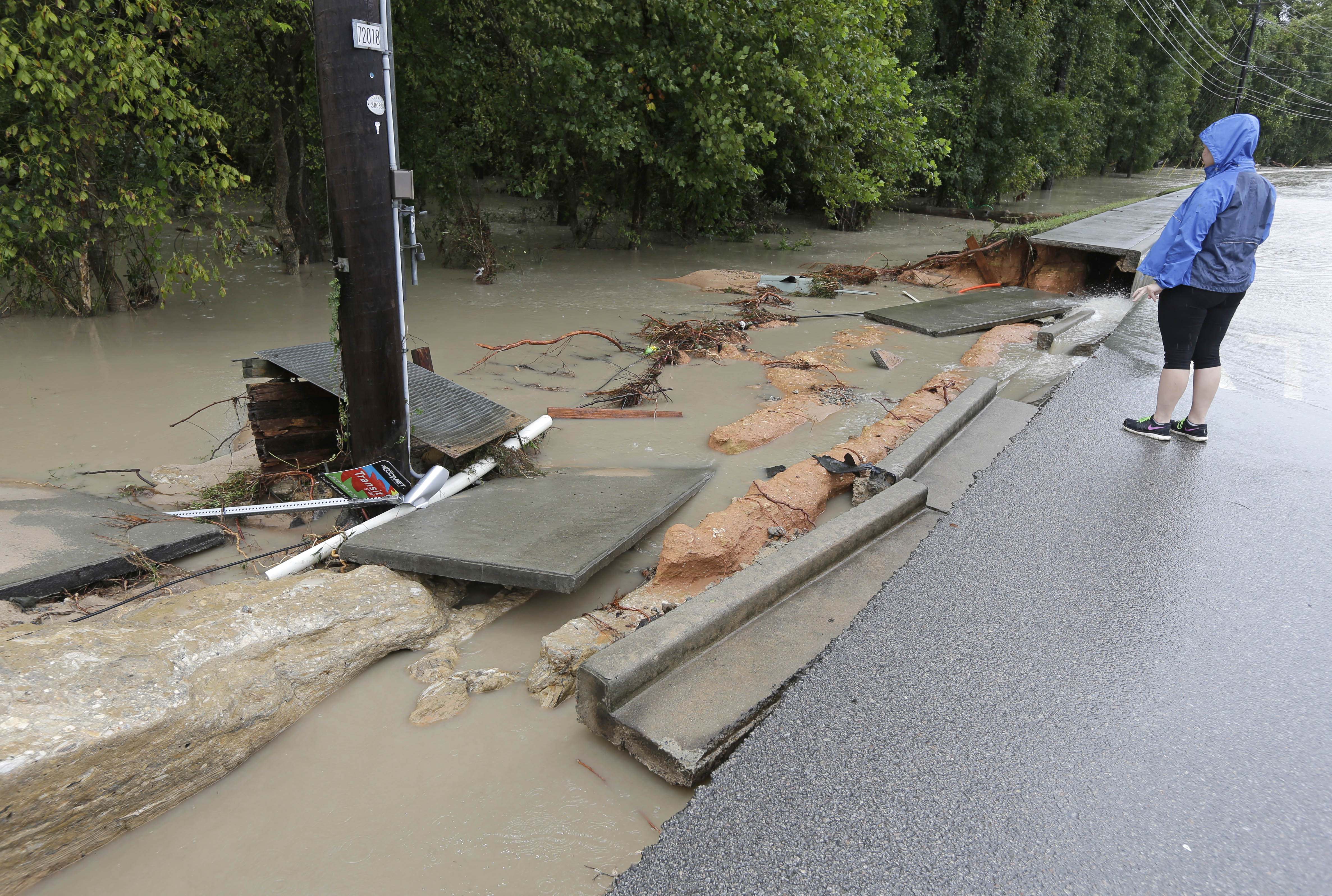 A woman looks at a section of a street washed away by floodwaters in Columbia, S.C., Sunday, Oct. 4, 2015. 