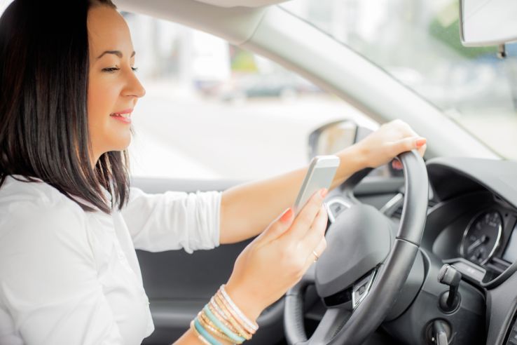 woman driving and looking at her smartphone