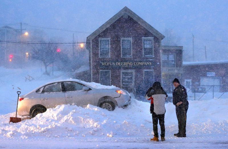 A police officer questions the driver an occupant of a car that ended up on top of a tall snowbank in the middle of Commercial Street during a blizzard in Portland, Maine.