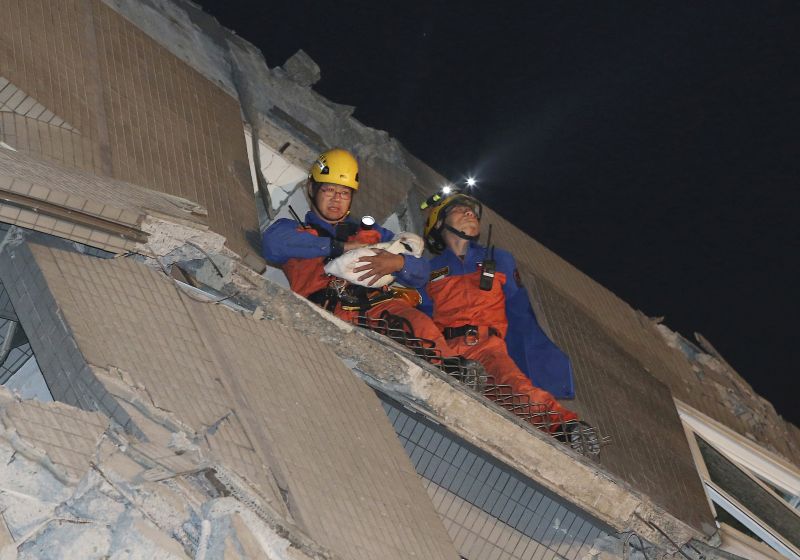 Rescue workers carry a baby swaddled in a cloth from the rubble of a toppled building after an earthquake in Tainan, Taiwan