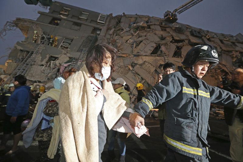A woman is led by a rescue worker from the site of a toppled building 