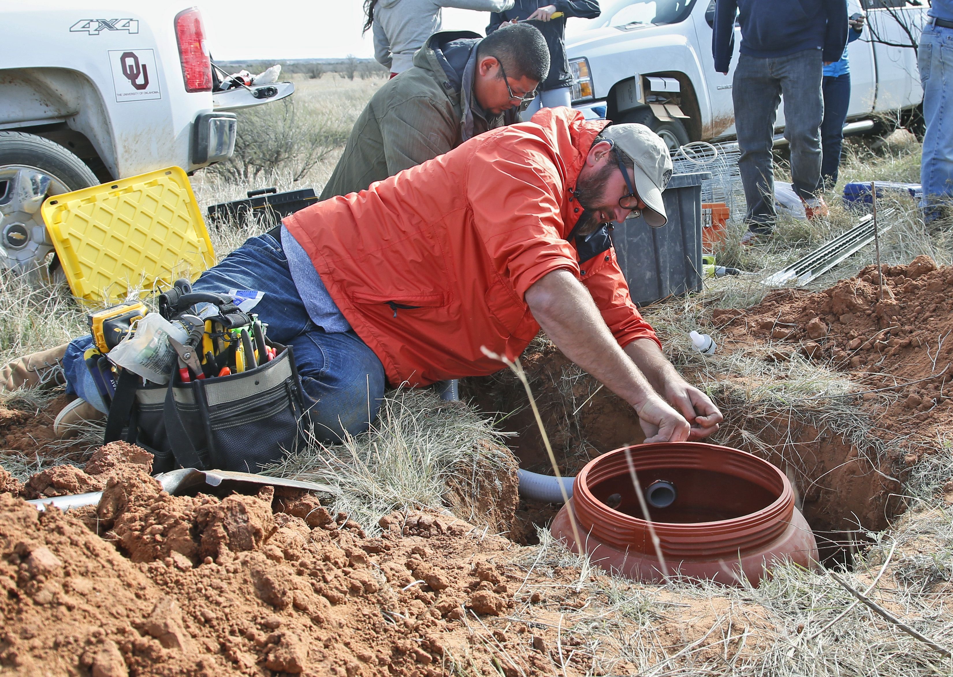 Joel Woelfel, front, a technician at the Oklahoma Geological Survey, prepares an in-ground container for a seismic monitor 