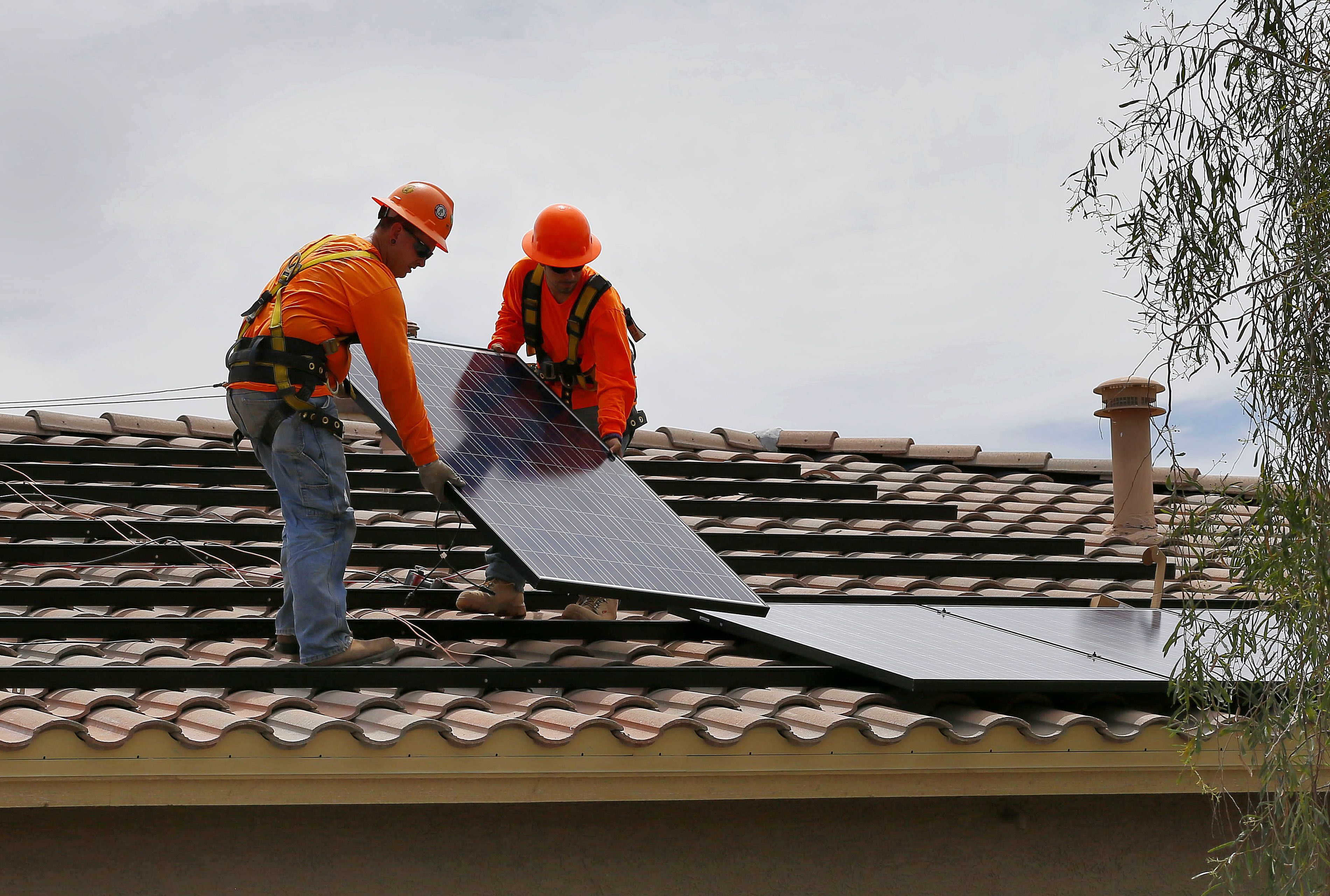 electricians Adam Hall, right, and Steven Gabert, install solar panels on a roof for Arizona Public Service company in Goodyear, Ariz. 