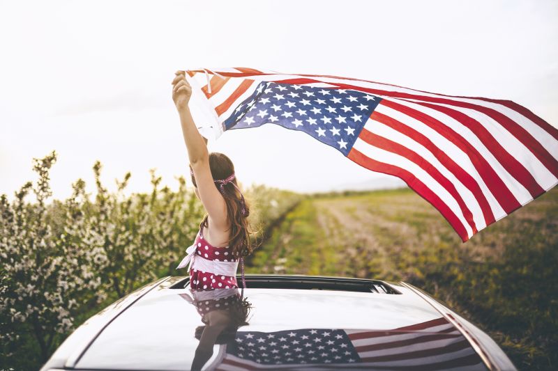 Girl holding an American flag out car sunroof in the wind