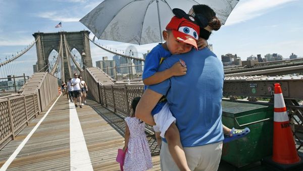 Xiuquin Huang carries her grandson Ruize Yan beneath an umbrella as she walks across the Brooklyn Bridge with her daughter and granddaughter Rina Wu, as excessive heat continued to blanket the Northeast on July 24. (Photo: Kathy Willens/AP Photo)