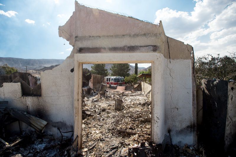 An exterior wall stands in front of a residence scorched by a wildfire