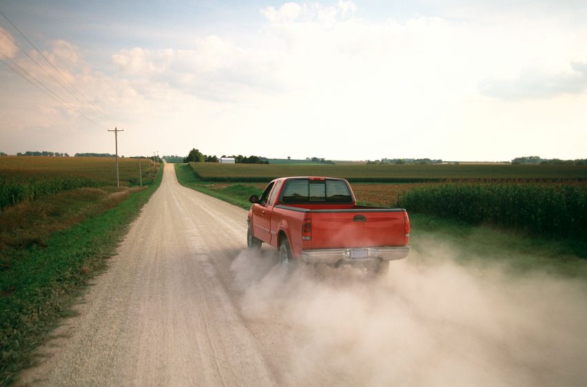 Red pickup driving down dirt country road