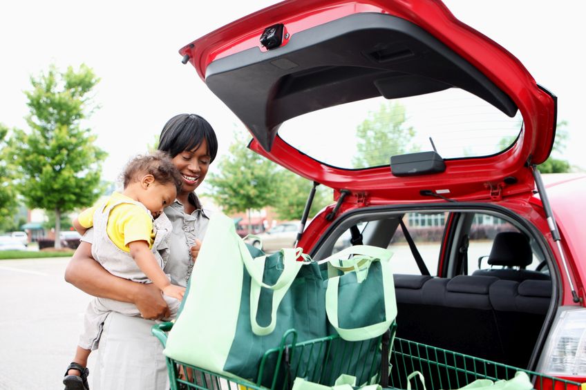 woman with infant placing groceries in red car