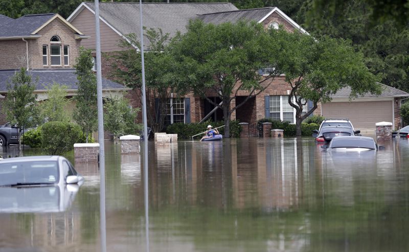 A person paddles through a flooded neighborhood
