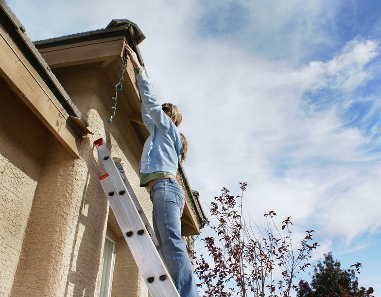 woman on ladder installing home holiday lights