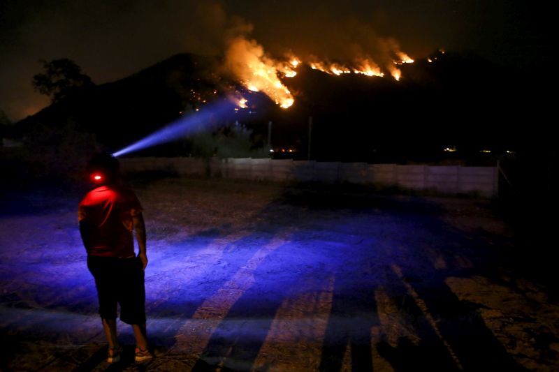 A youth wearing a head lamp watches a forest fire rage on a mountain in Cajon del Maipo