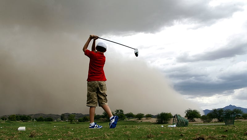 Young man on driving range in sand storm in Arizona
